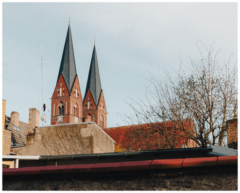 A photograph of a church's two towers peeking over a wall and the tops of residential buildings.