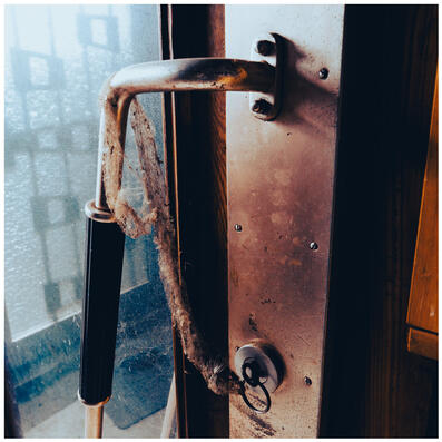 A photograph of a 1930s-ish door handle, with spiderwebs and dirt hanging off it in a string connecting to a key in the lock.