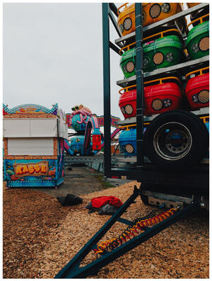 A photograph of yellow, green, and red carnival ride cars on a lorry. The attraction they'll go on to, an octopus-style(d) ride, is in the background.